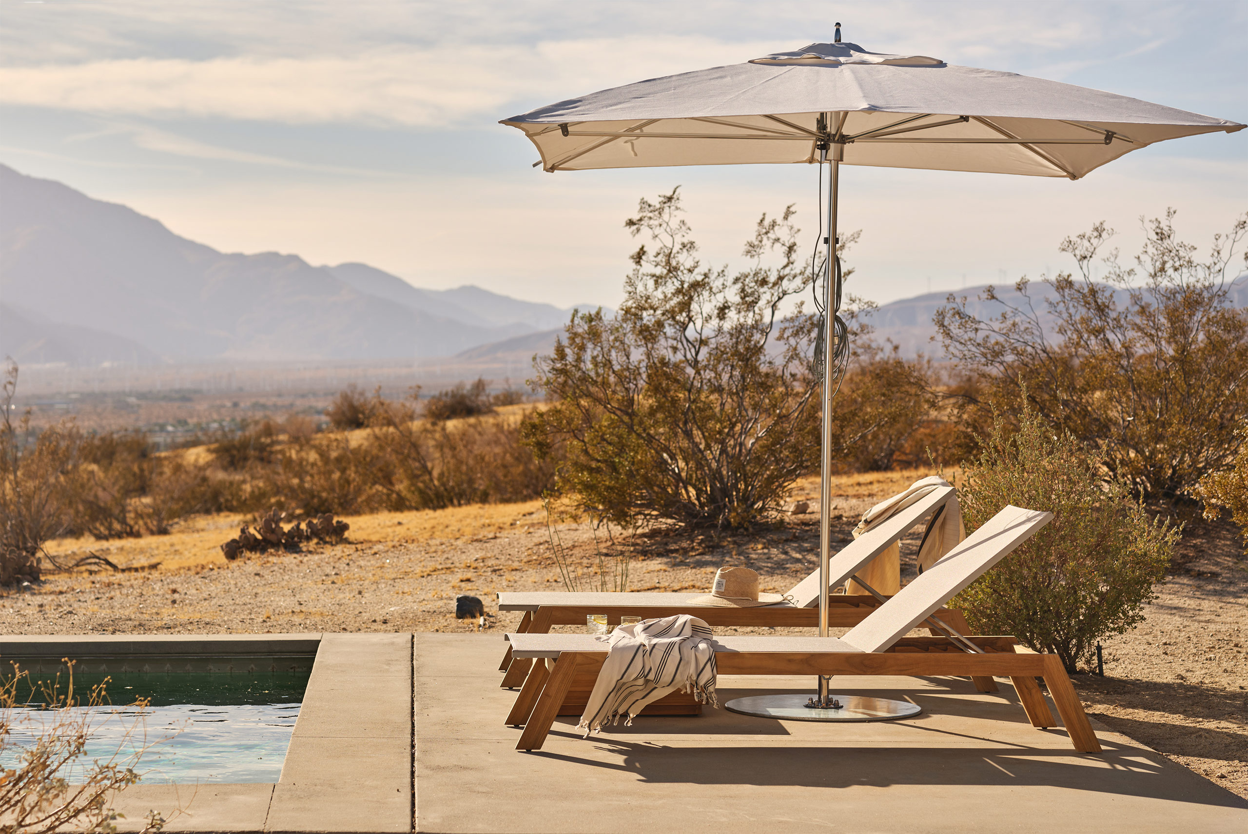 Tiburon teak sling chaise under a TUUCI umbrella in desert environment